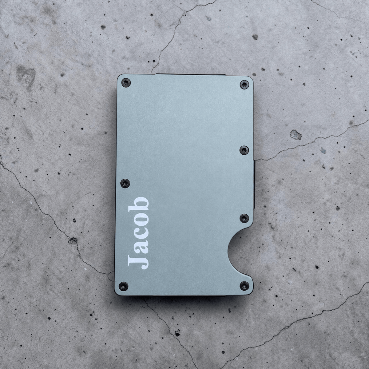 Light blue personalised metal card holder with engraved name on a concrete surface