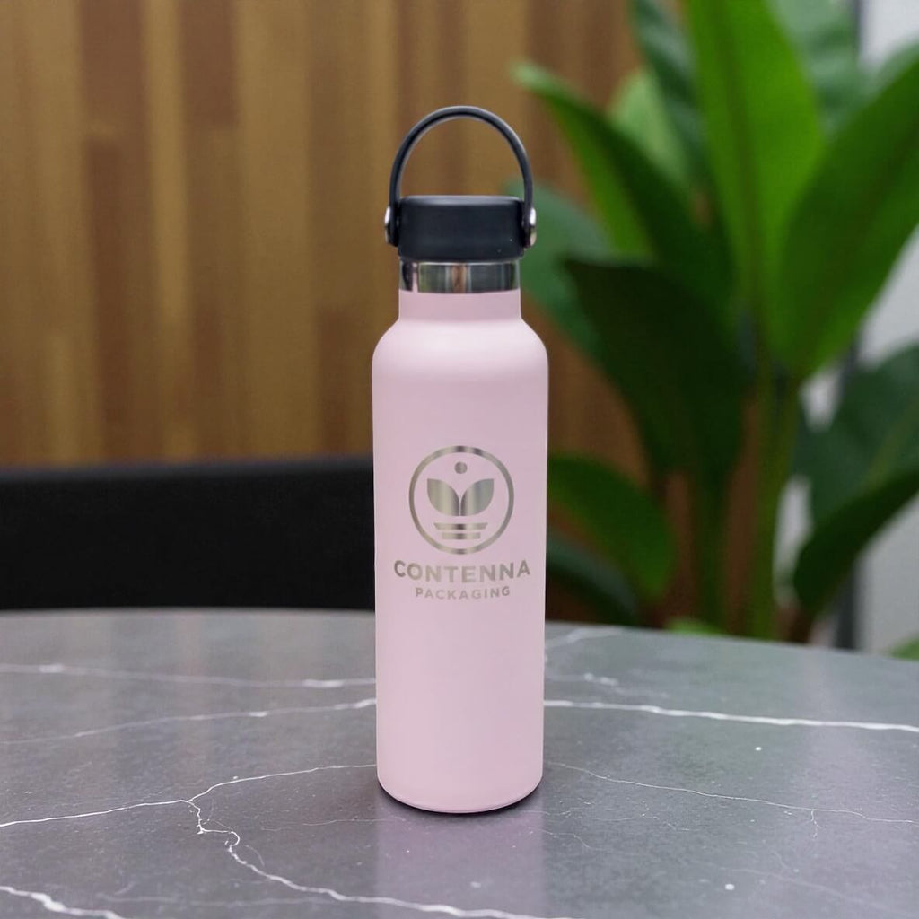 Light pink stainless steel water bottle with engraved company logo and carry handle lid on marble tabletop.