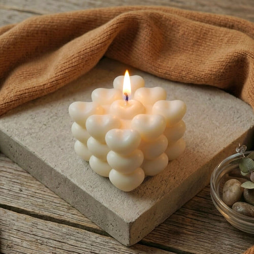 Lit handmade heart cube scented soy candle burning with warm flame on concrete block, unique bubble cube candle gift for her