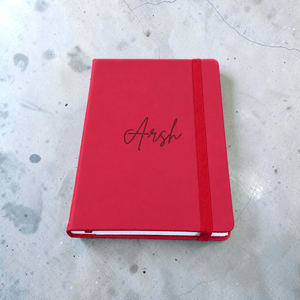 Maroon PU leather journal with Arsh engraved in cursive, showcasing a custom name notebook for writing and journaling, placed on a light gray concrete surface.