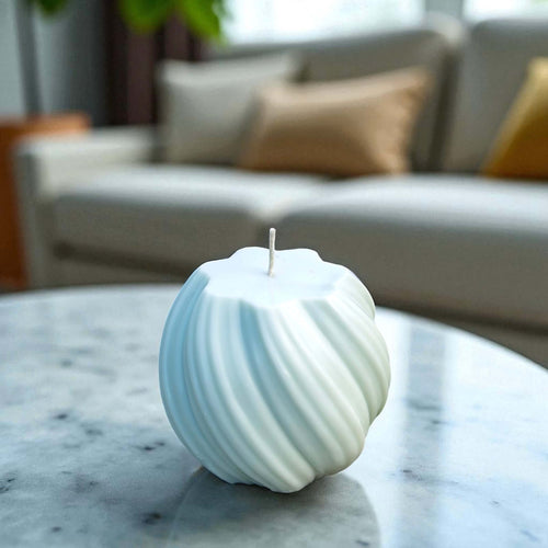 Minimalist white swirl ball candle with textured grooves, placed on a marble coffee table in a cosy lounge.