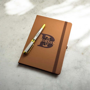 Notebook with engraved floral letter 'D' and name, styled on a marble surface with personalised pen across the top