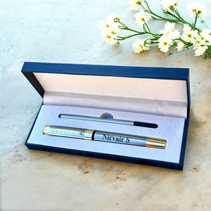 Pen with personalised name in a black box on a light surface with flowers.