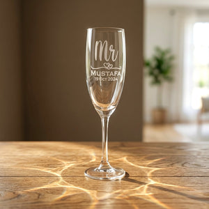 Personalised Mr champagne flute engraved with groom's name Mustafa and wedding date 19 Oct 2024 on a wooden table