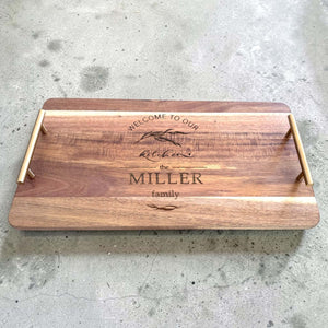 Personalised acacia wood serving platter engraved with a botanical kitchen design and custom family name, photographed from a slight elevation