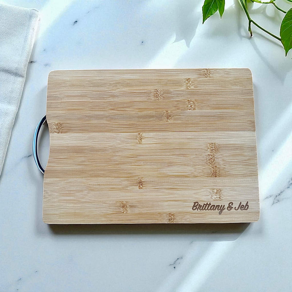 Personalised bamboo chopping board engraved with couple’s names on marble countertop.