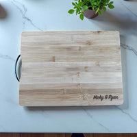 Personalised bamboo chopping board engraved with couple’s names on marble countertop.