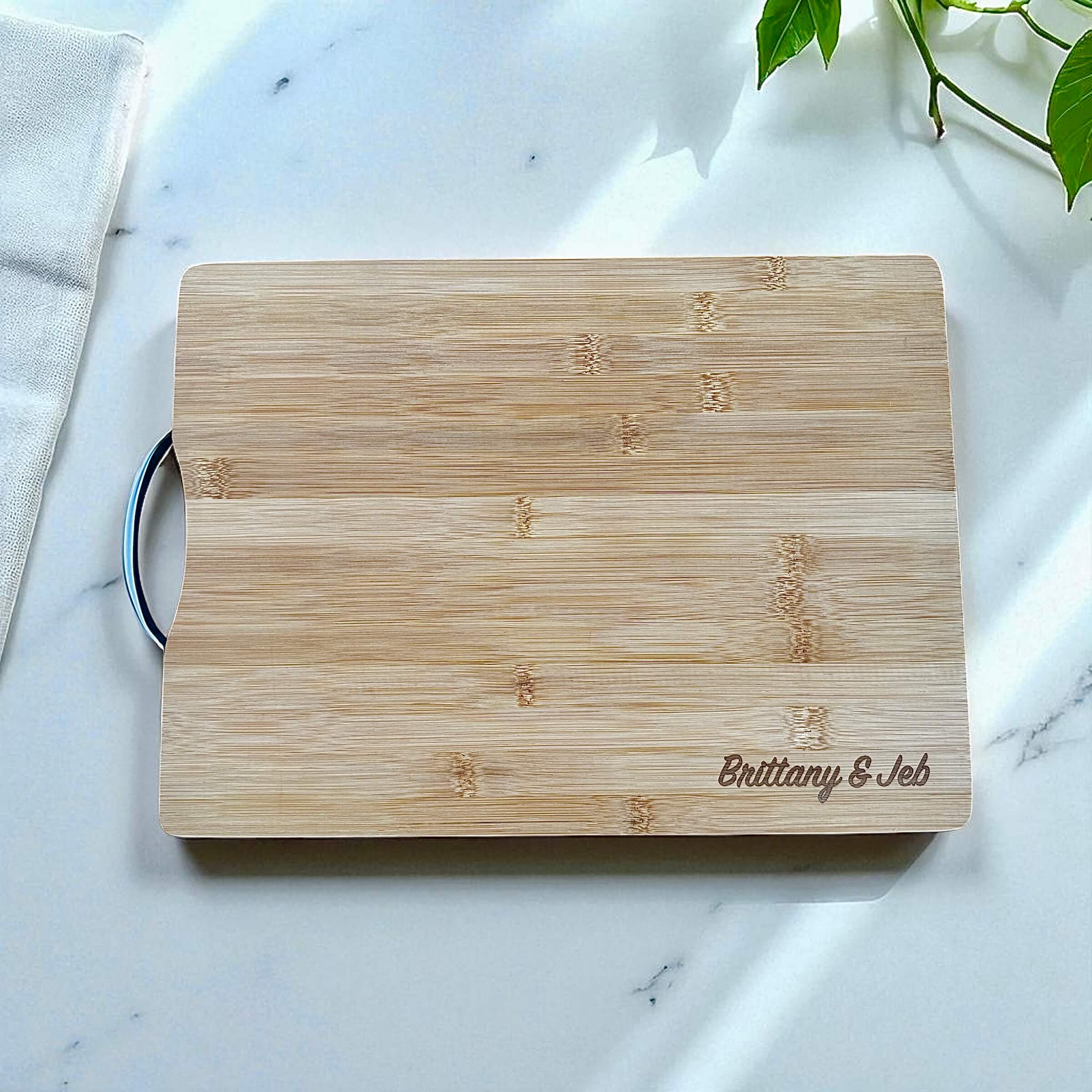 Personalised bamboo chopping board engraved with couple’s names on marble countertop.