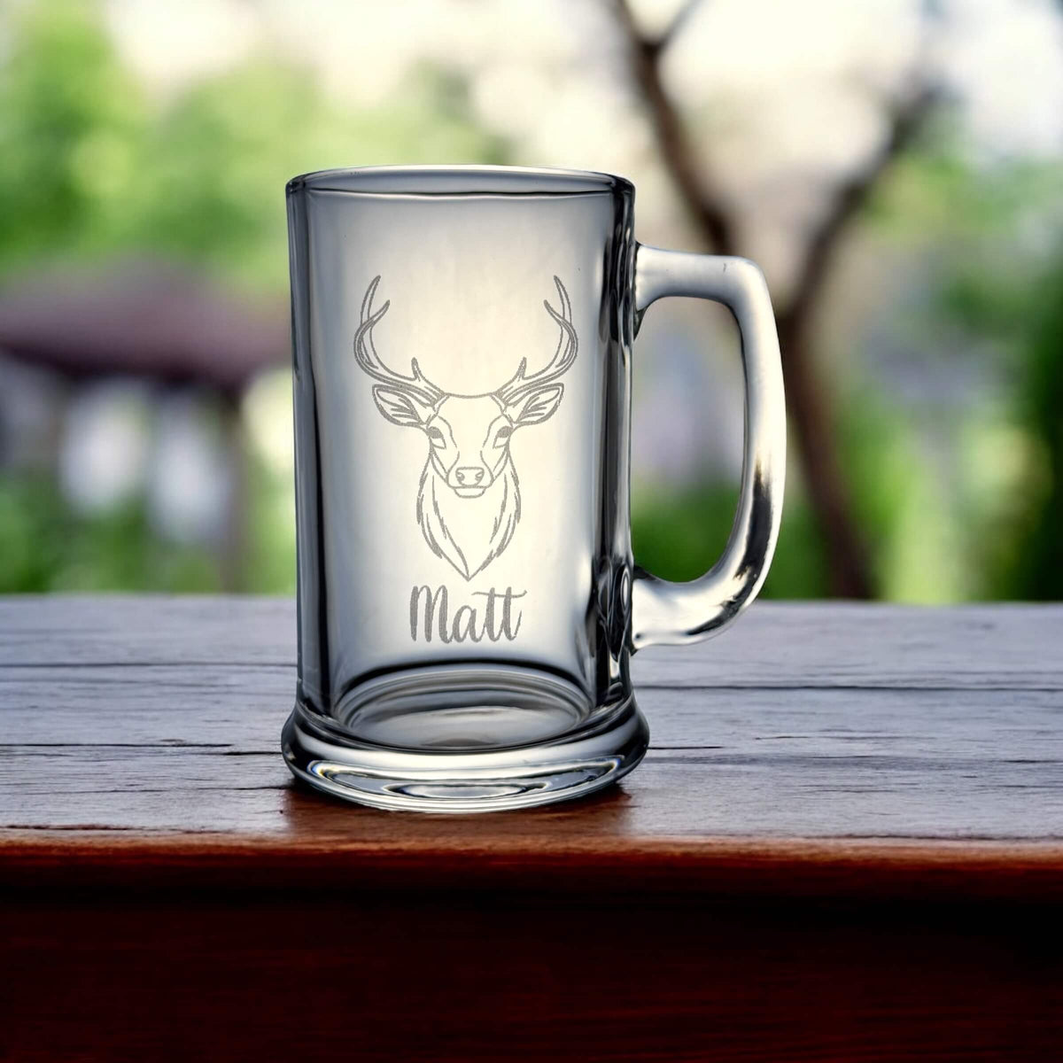 Personalised beer glass with engraved stag and name “Matt” on a wooden surface outdoors.