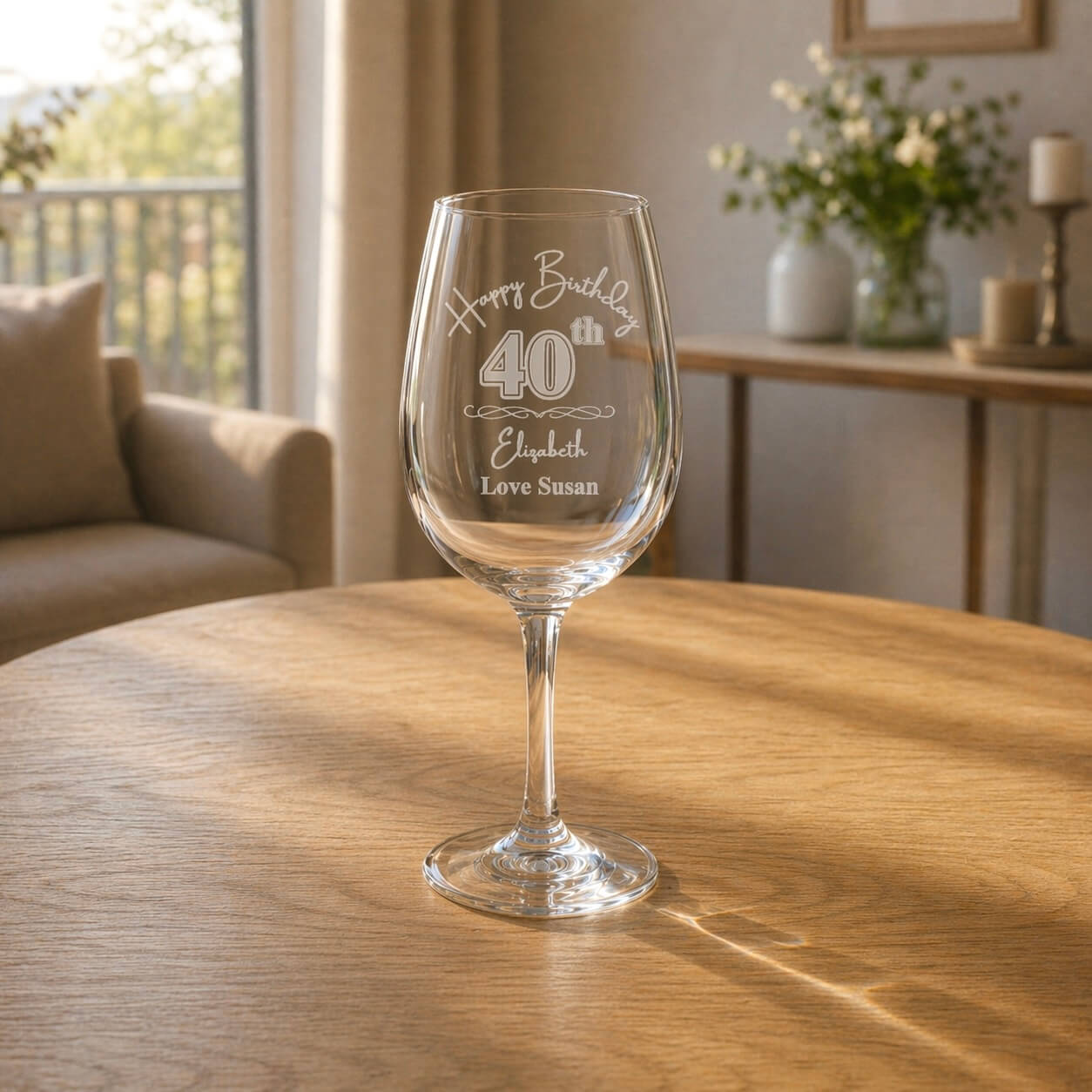 Personalised birthday wine glass with custom 40th engraving and name, displayed on a round wooden table with a styled home interior background