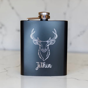 Personalised black hip flask with engraved stag head design and Jithin name on marble background