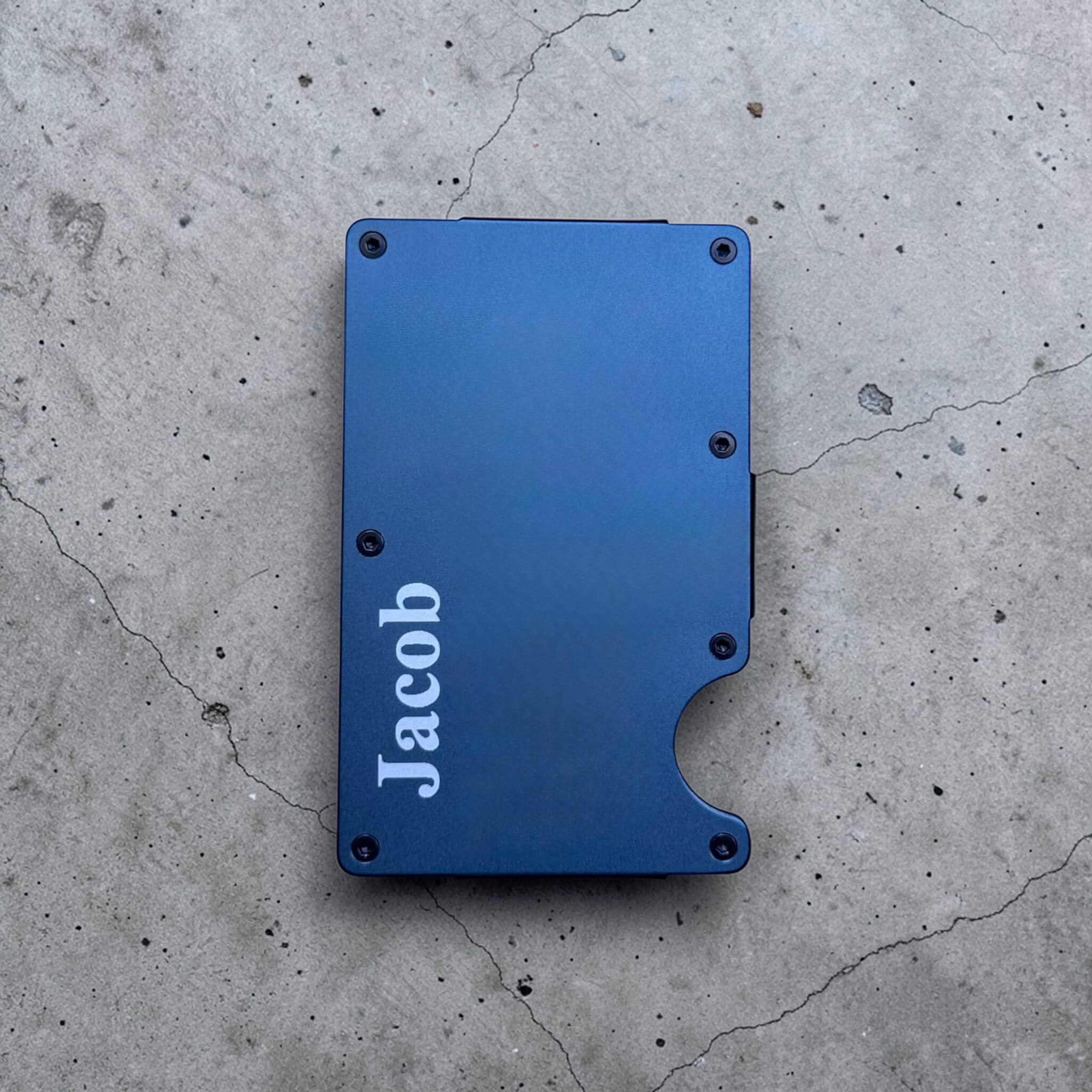 Personalised blue aluminium slim card holder with custom engraved name on concrete surface, minimalist RFID wallet gift for him