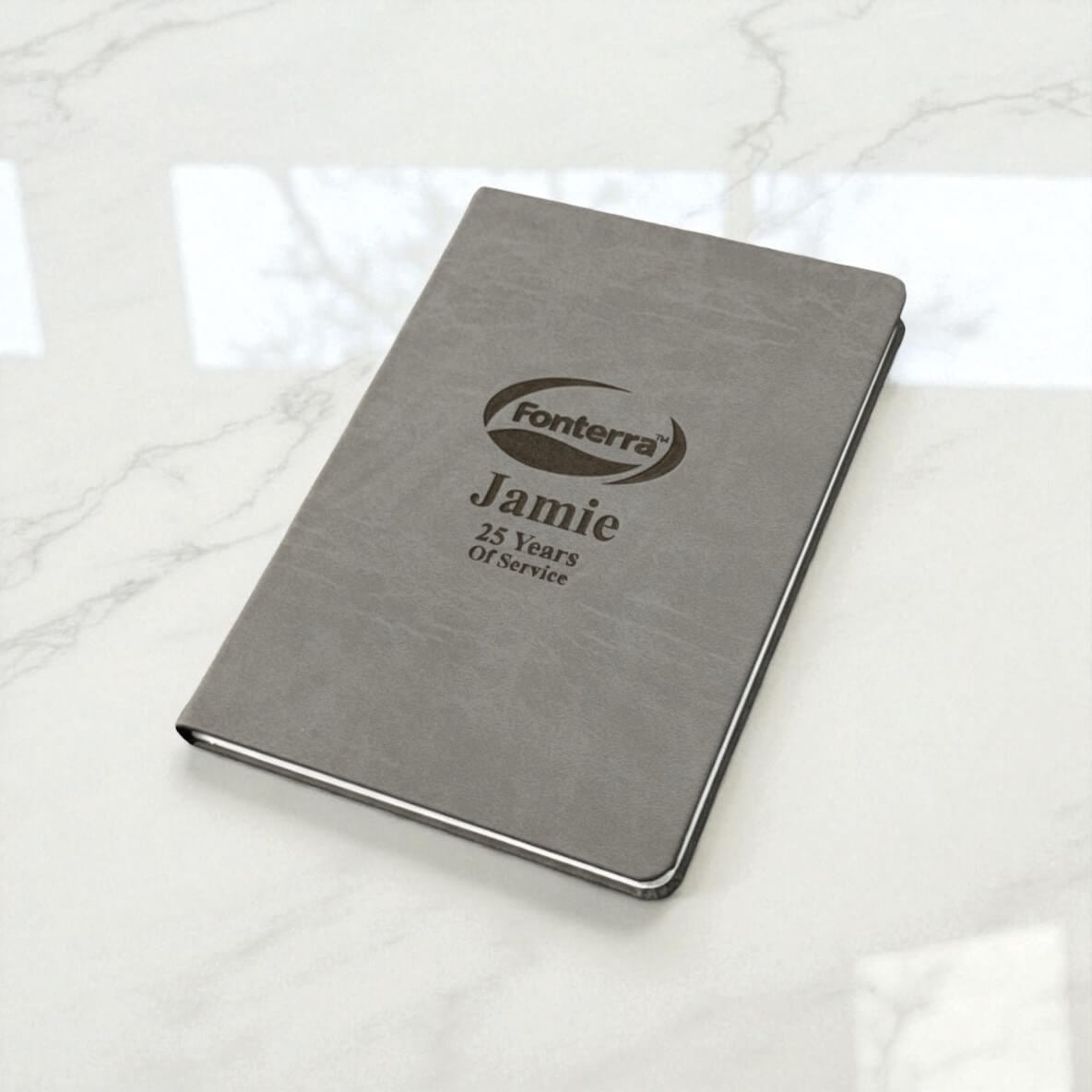 Personalised company logo journal on marble surface, engraved with name and years of service, an elegant business gift for NZ employees.