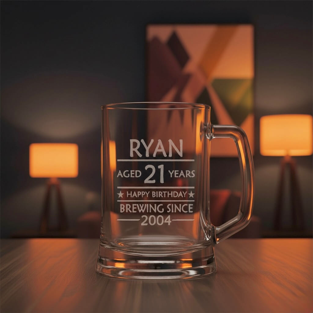 Personalised engraved beer mug with text “Ryan Aged 21 Years Happy Birthday Brewing Since 2004” on wooden table with warm lights