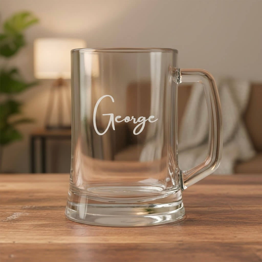 Personalised glass beer mug engraved with the name George, displayed on wooden table in warm home setting