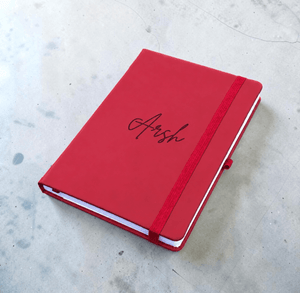 Personalised maroon notebook with custom Arsh name engraving, elastic closure and lined journal pages visible from the front.