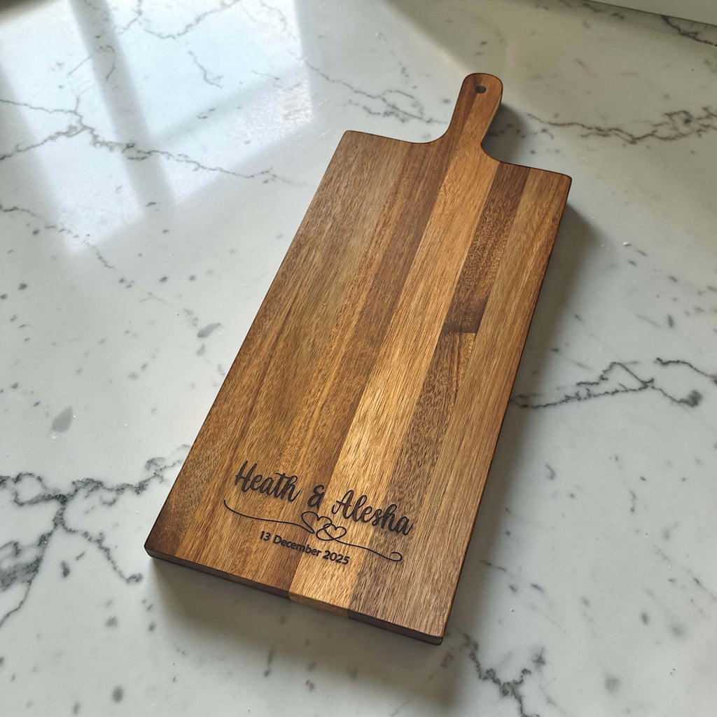 Personalised rectangular acacia wood wedding serving board laser engraved with couple names and wedding date, on marble surface