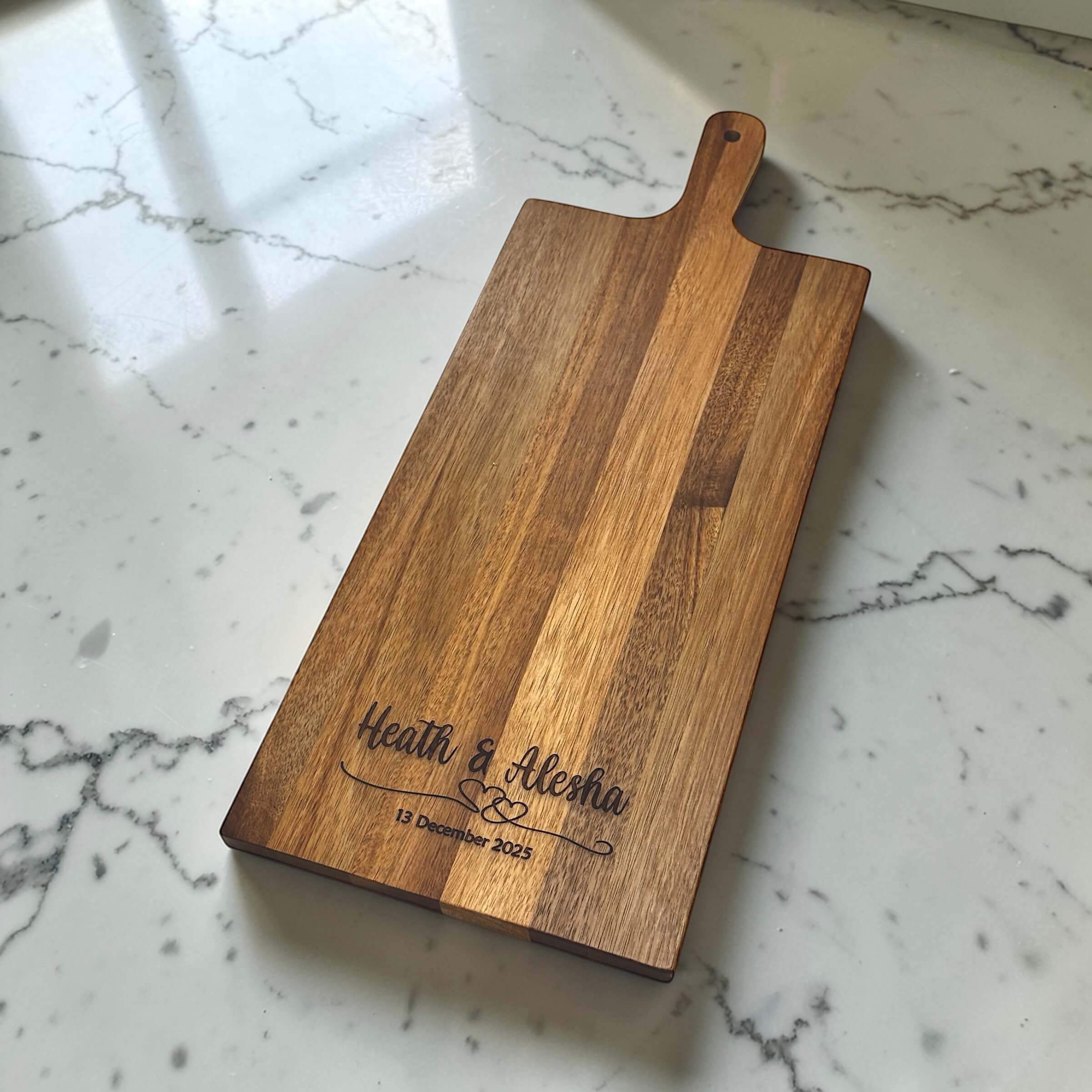Personalised rectangular acacia wood wedding serving board laser engraved with couple names and wedding date, on marble surface