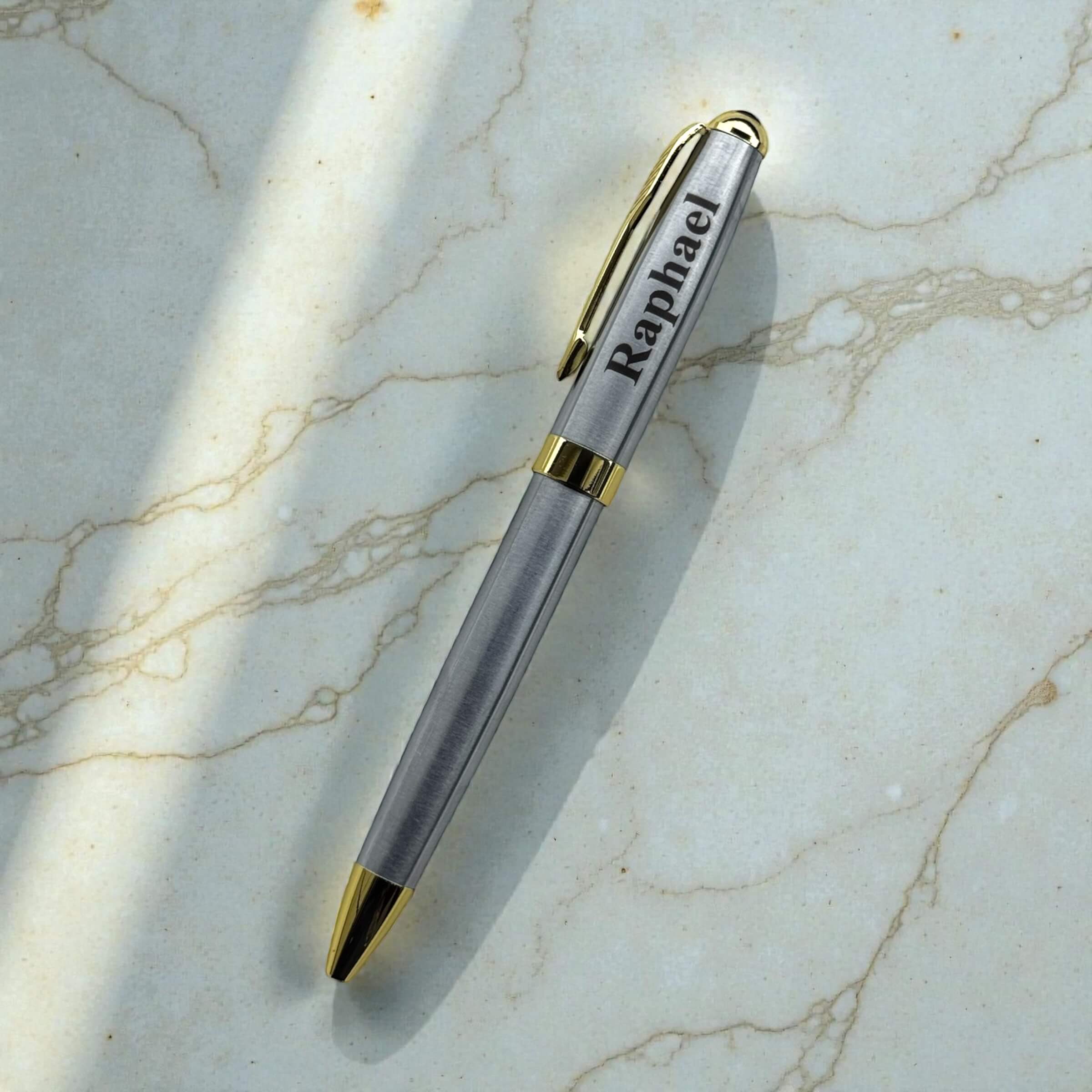 Personalised silver pen with gold accents on a marble surface engraved with name "Raphael"