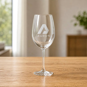 Personalised wine glass engraved with the Auron company logo, sitting on a wooden table in a bright home setting
