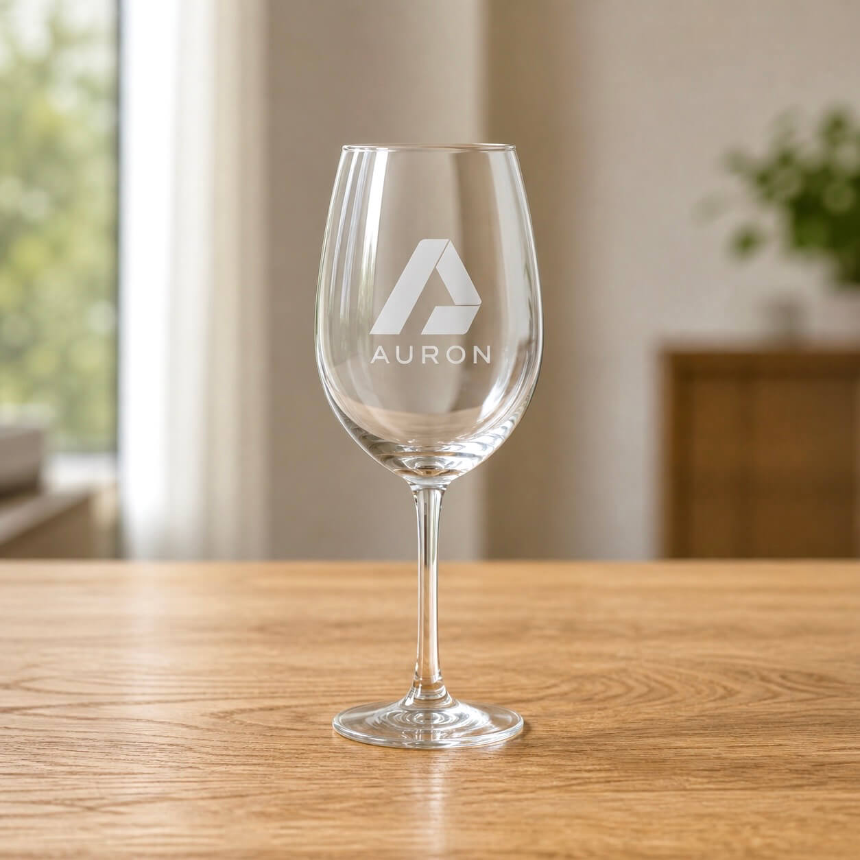 Personalised wine glass engraved with the Auron company logo, sitting on a wooden table in a bright home setting