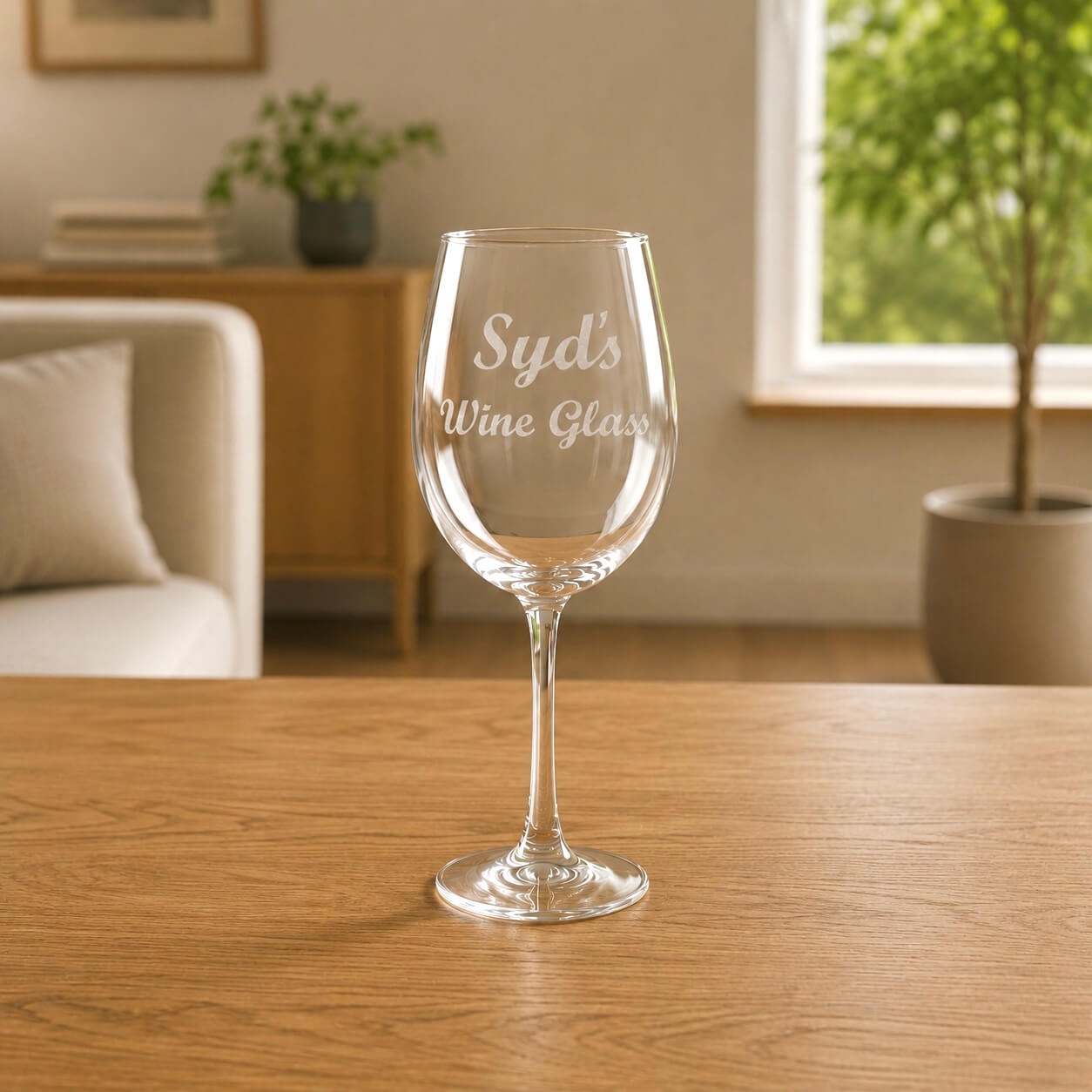 Personalised wine glass engraved with the name Syd in a script font, sitting on a wooden table in a cosy living room setting