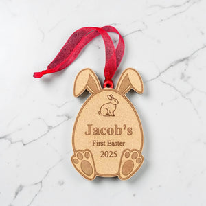 Personalised wooden first Easter ornament tag engraved with child's name and year, Easter bunny egg shape with red ribbon on marble