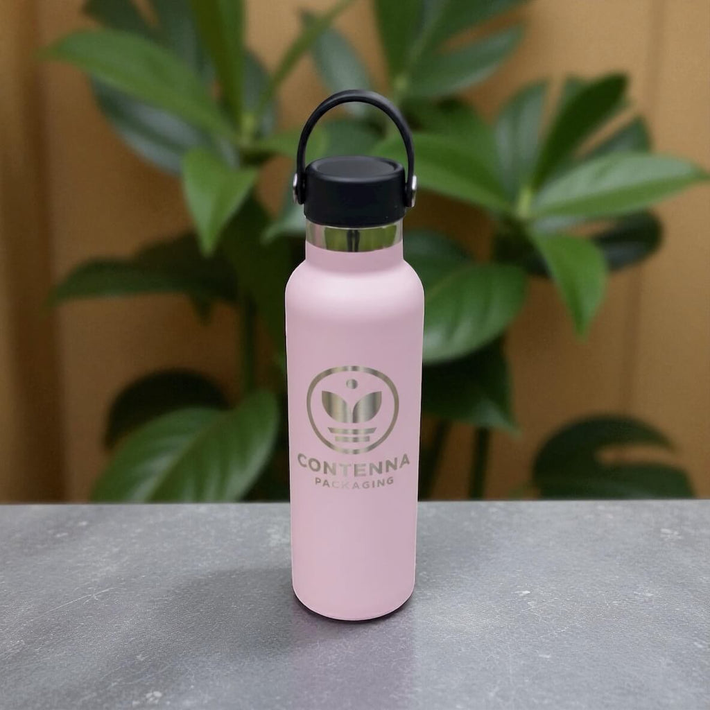 Pink engraved stainless steel drink bottle shown upright on dark stone surface with plants in background.