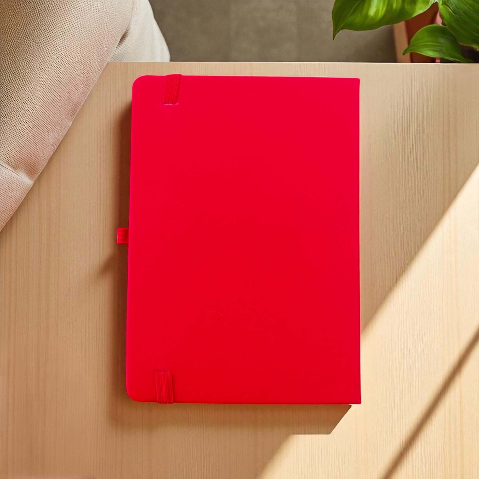 Red notebook on a wooden surface with a plant in the background