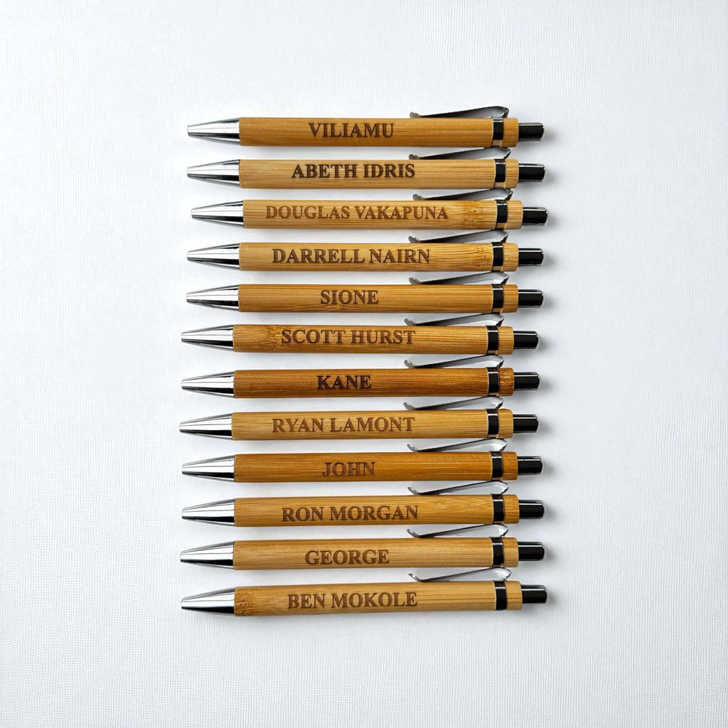 Row of engraved bamboo pens with custom names, featuring natural wood finish and metal tips.