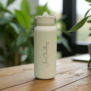 Sage 1L stainless steel water bottle personalised with engraved name, displayed on a wooden table with plants in the background.