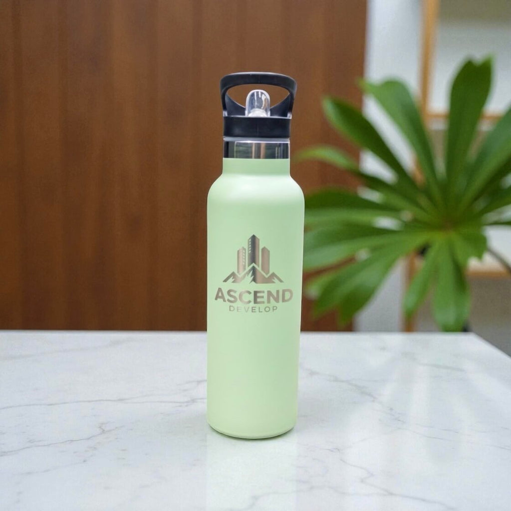 Sage green stainless steel water bottle with engraved corporate logo displayed upright on white marble tabletop.