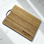 Side angle of engraved bamboo chopping board with stainless steel handle, personalised for corporate gifting.