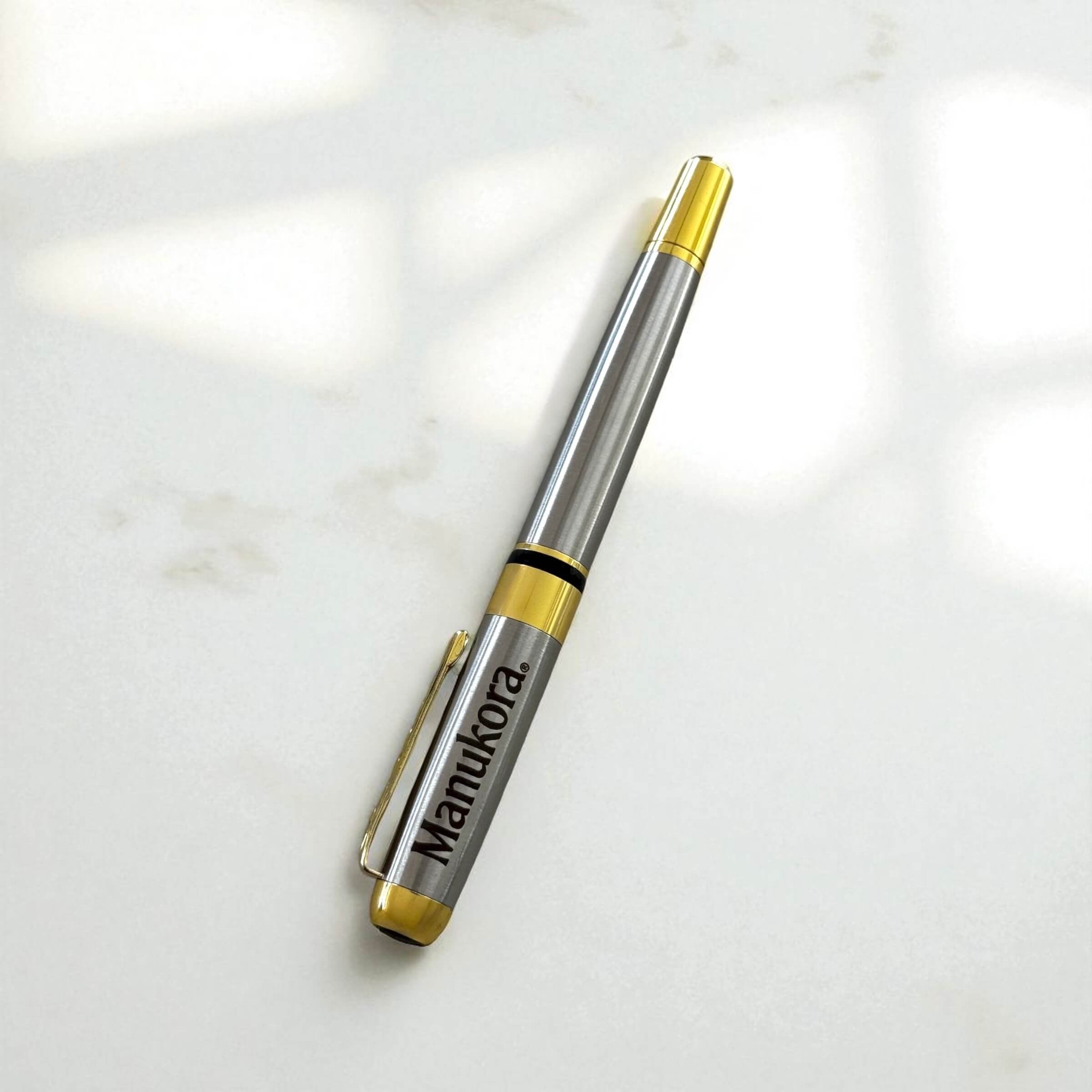 Silver-tone metal pen with gold accents engraved with logo, displayed on marble surface.