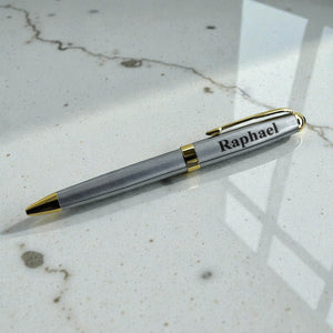 Silver and gold custom name pen shown on a light textured surface with laser engraving