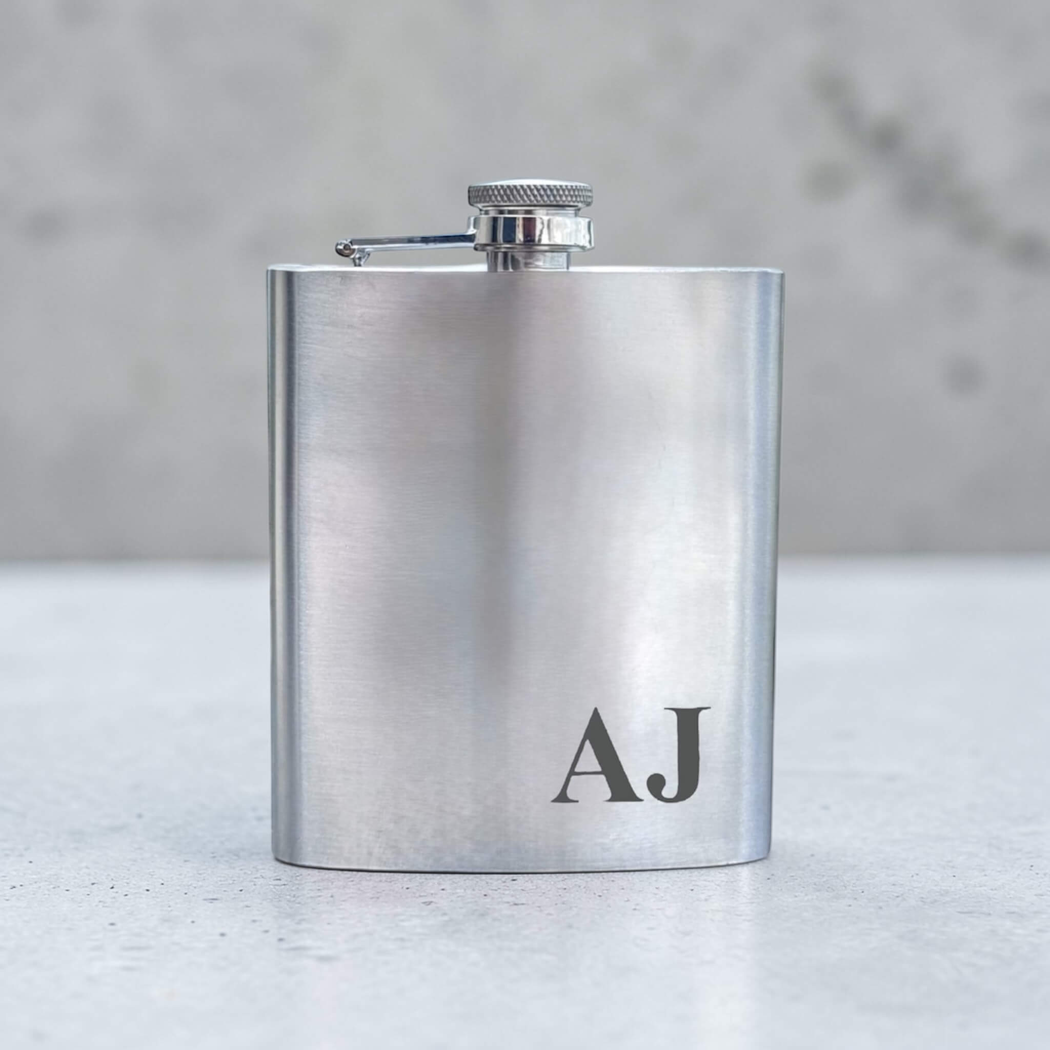 Silver flask with 'AJ' engraving on a light surface