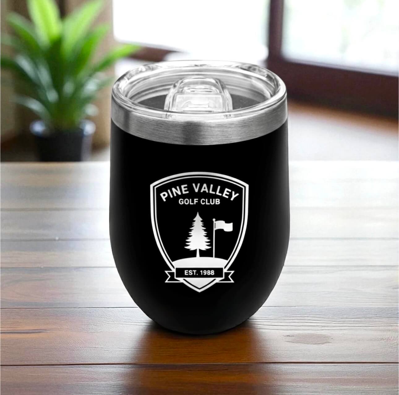 Sleek black coffee cup with engraved logo and lid attached, displayed on modern office desk.
