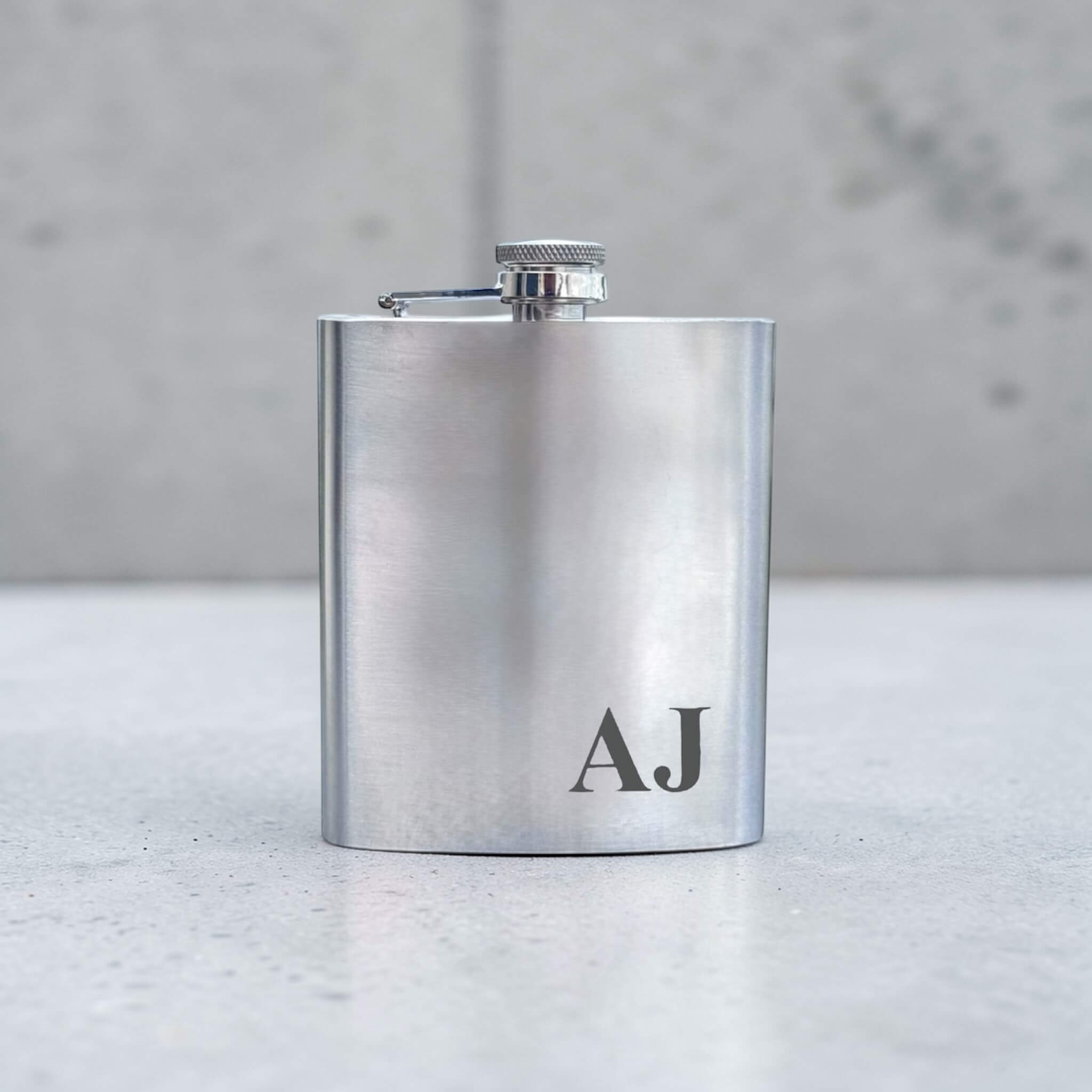 Stainless steel flask with 'AJ' initials engraved on a marble surface