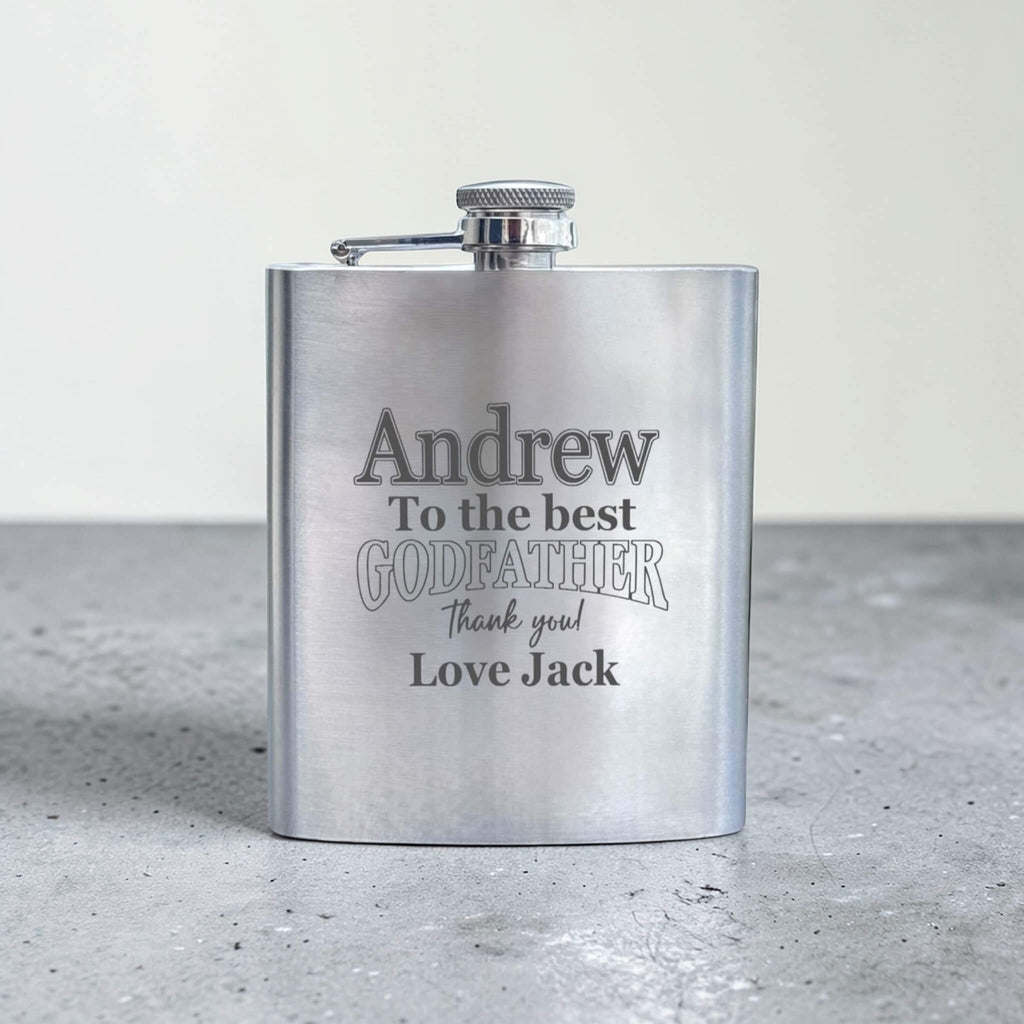 Stainless steel flask with engraved text for godfather on a gray surface
