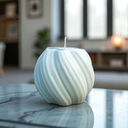 Textured sphere candle with spiral design in clean white, positioned on a reflective marble surface.