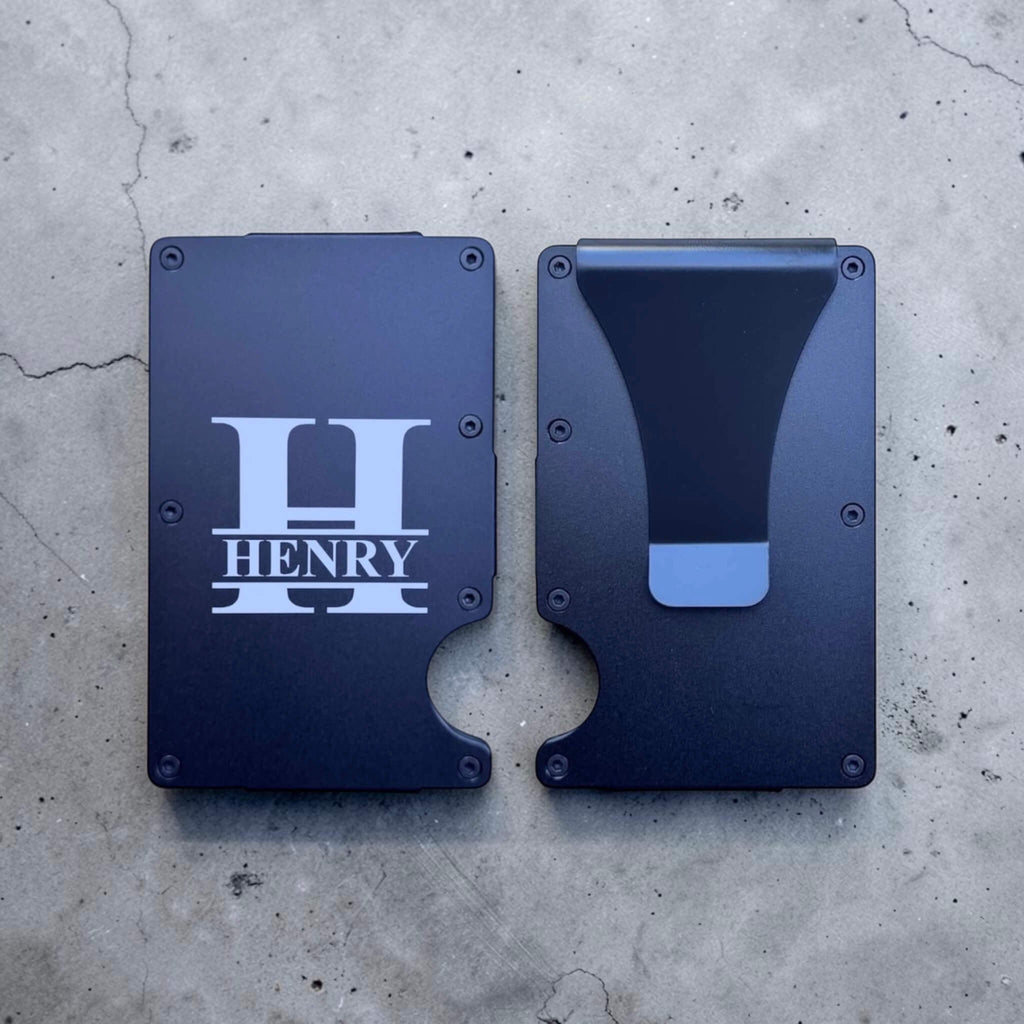 Two Blue personalised aluminium card holder featuring a large initial with the name engraved inside on a concrete surface