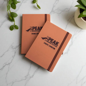 Two Tan leather personalised business journals engraved with name and logo, styled on marble desk.