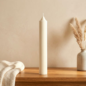 Unlit soy wax candle with a tall sculptural shape beside simple neutral decor