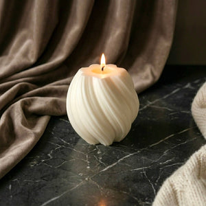 White textured scented soy candle burning on a dark marble surface with brown fabric in the background