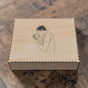 Wooden box with a engraved illustration of a father holding a baby on a wooden surface