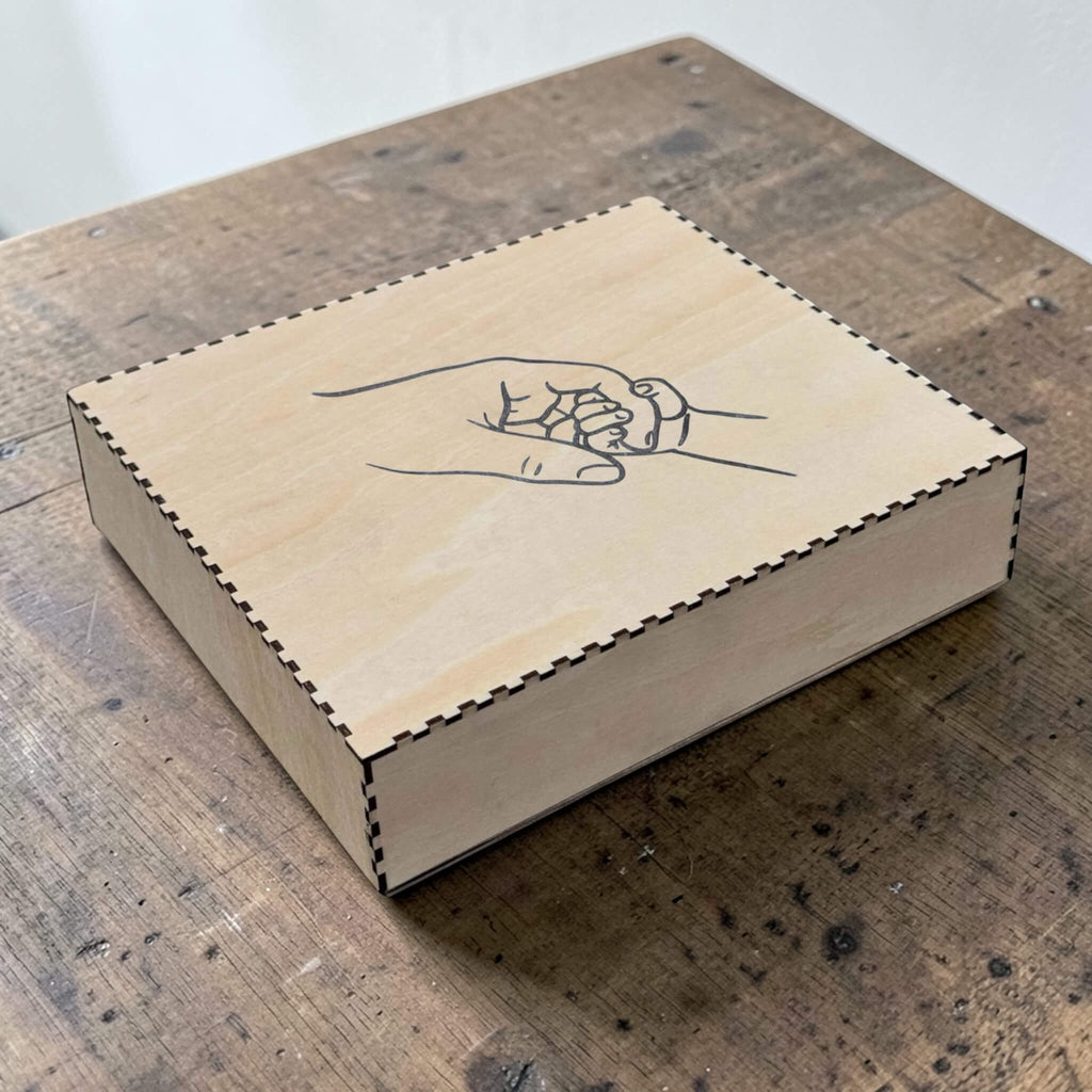 Wooden box with a hand design of two hands holding each other on a wooden surface.