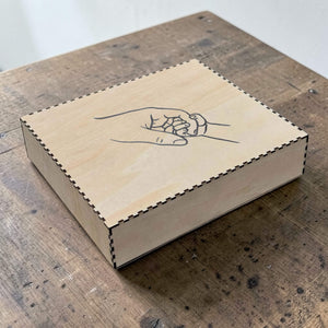 Wooden box with a hand design of two hands holding each other on a wooden surface.