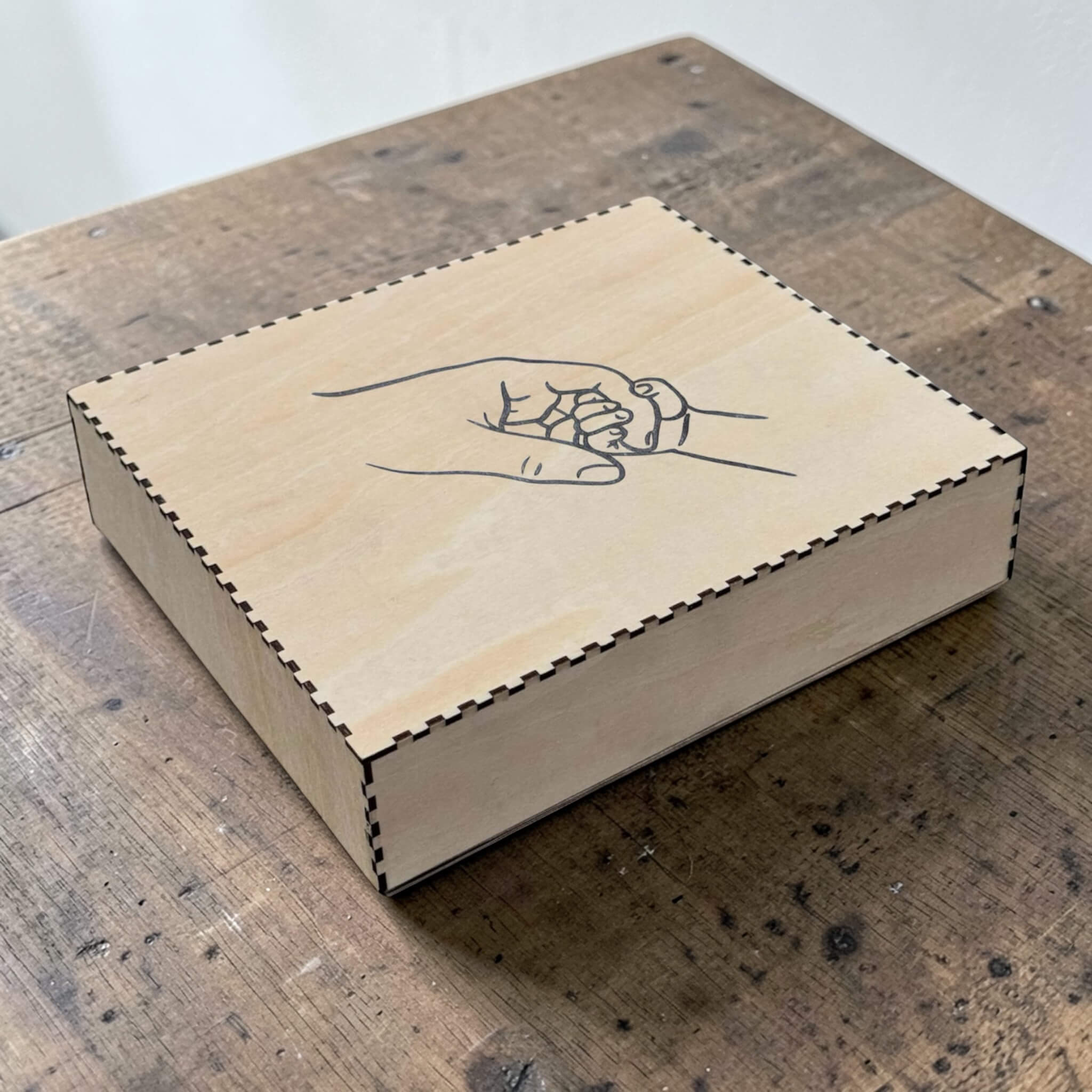 Wooden box with a hand design of two hands holding each other on a wooden surface.