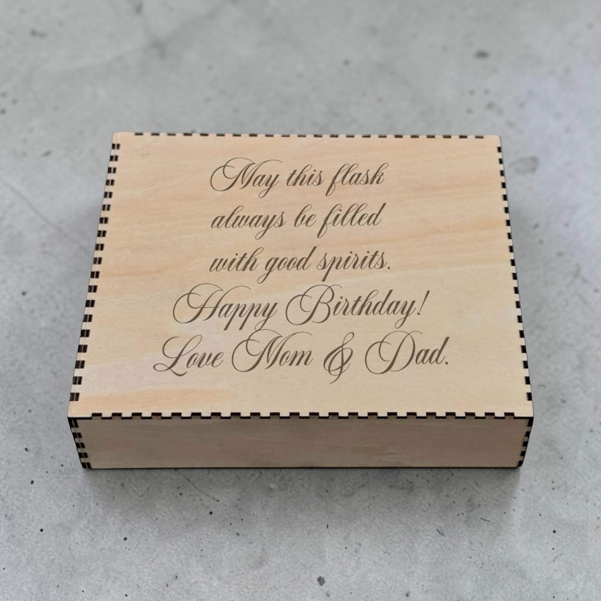 Wooden box with engraved birthday message on a concrete surface