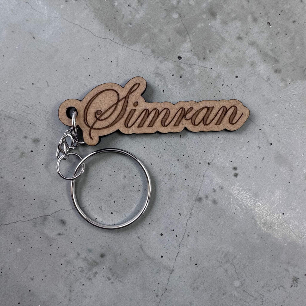 Wooden keychain with 'Simran' engraved on a concrete surface